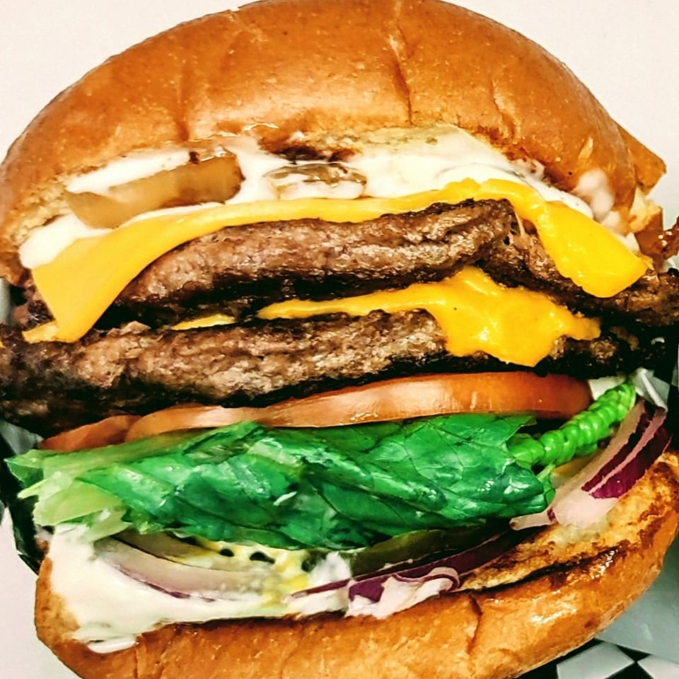 A close-up of a double cheeseburger from Springdale Cafe with lettuce, tomato, onion, and sauce.