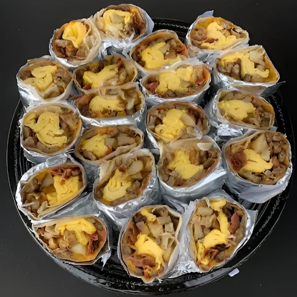 A catering tray filled with many breakfast burritos, each wrapped in foil and open at the top.