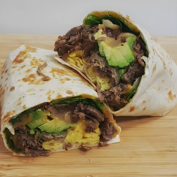 A Springdale Cafe breakfast burrito, cut in half, revealing steak, avocado, scrambled eggs, and greens.