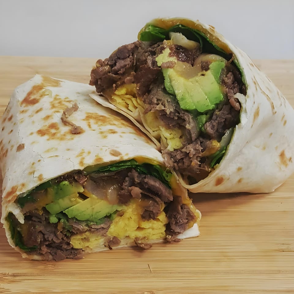 A Springdale Cafe breakfast burrito, cut in half, revealing steak, avocado, scrambled eggs, and greens.